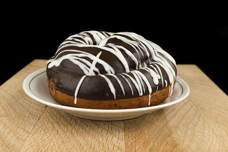 巧克力木板摄影照片_面包上覆盖着巧克力，放在白盘子里，放在木板上，黑色背景