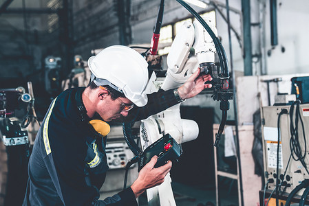 熟练工人摄影照片_年轻的工厂工人与熟练的机械臂一起工作
