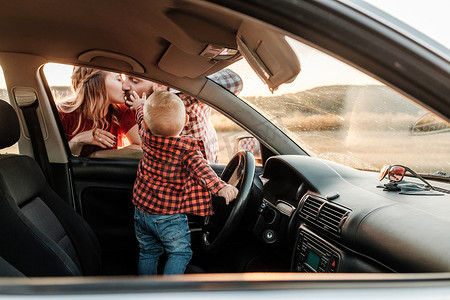 快乐的年轻家庭妈妈和爸爸带着他们的儿子小司机在阳光明媚的日落、假期和公路旅行概念下在城外的车上享受夏日周末野餐