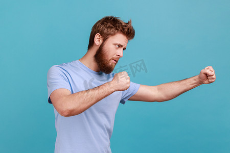 身穿蓝色T恤的男子站着拳击拳头，准备进攻或防守，表情愤怒