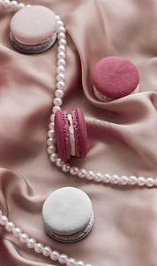 丝绸珠宝摄影照片_丝绸背景上的甜马卡龙和珍珠首饰、巴黎别致珠宝、法式甜点食品和豪华糖果品牌的蛋糕马卡龙、节日礼物