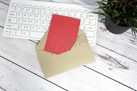 棕色信封内的红色便条，配有键盘和木桌上的盆栽植物。