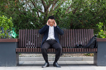人累了摄影照片_亚洲商人下班后累了，坐在长凳上，疲倦头痛
