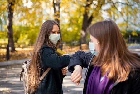 校园安全摄影照片_戴着医用防护口罩的女学生朋友用肘部互相问候