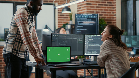 程序员在配有多个计算机屏幕和带有绿屏色度键模型的笔记本电脑的办公桌前工作