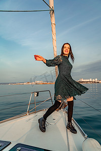 阳光明媚的夏日，女人站在游艇的鼻子上，微风吹拂着头发，背景是美丽的大海