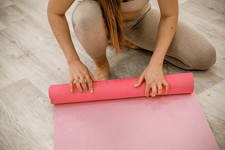 双11预热摄影照片_在家瑜伽的女人在客厅里滚动粉红色的运动垫，开始为冥想禅宗健康生活方式客厅公寓预热。