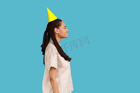 戴着派对锥帽的女人的侧视图，带着露齿的微笑看着相机，欢庆庆祝活动。