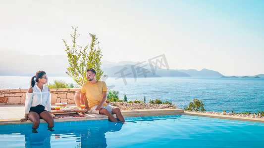 度假期间，一对男女在泳池边吃早餐，眺望大海