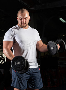 健美运动员摄影照片_男性健美运动员在健身房使用哑铃