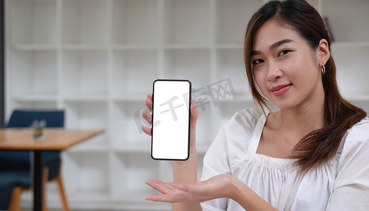 一位笑脸亚洲美女手持并展示带有空白屏幕的黑色手机的模型图像。