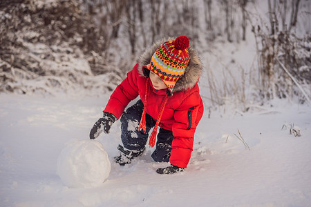 穿着红色冬装的可爱男孩在堆雪人。