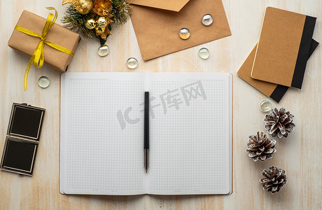 牛皮纸信封摄影照片_米色木质背景上的白色开放记事本、牛皮纸信封和圣诞装饰