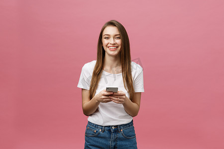 一张欢快可爱的美丽年轻女子在粉红色墙壁背景下用手机聊天的照片。