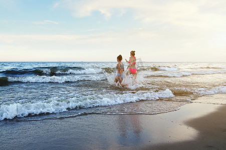 穿着泳装的女孩正在沙滩上玩海浪-跳跃、奔跑、玩乐。