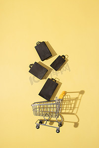 黄色背景黑色星期五销售中带购物袋的平躺式微型超市推车