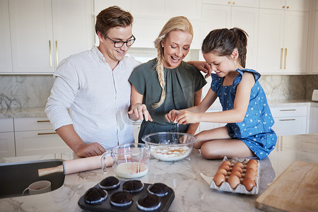母亲、父亲和女孩在厨房里作为一个幸福的家庭烘焙，一起享受美好的时光和周末。