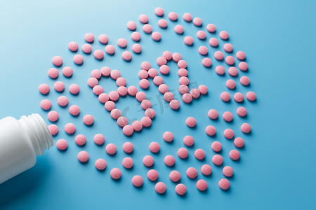 蓝色背景中心脏中维生素 B12 形式的粉红色药片，从白色罐头低对比度中溢出