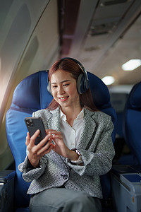 一位成功的亚洲女商人在飞机上的肖像坐在商务舱座位上，在飞行过程中使用智能手机播放音乐，relex 概念