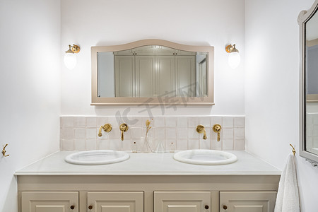 浴室以米色装饰，配有两个水槽、金色水龙头和复古镜子。
