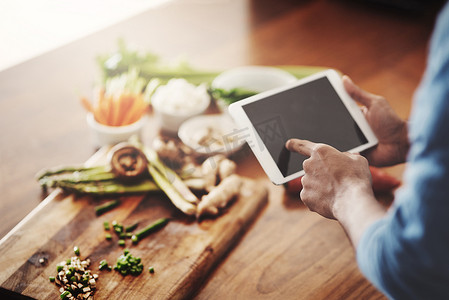 在做晚餐、午餐或早餐时，手持平板电脑研究健康食谱、观看烹饪教程视频和在线滚动寻找膳食创意的人的手特写。