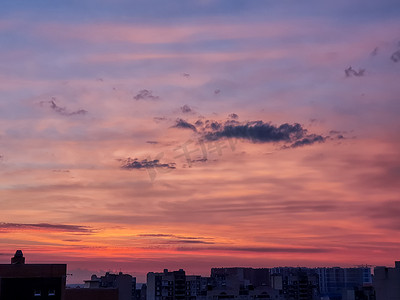 夕阳落下摄影照片_日落背景与美妙的红色、金色、黄色的天空，令人惊叹的紫色和橙色的天空在晚上太阳从城市上空落下时。戏剧性的日落天空