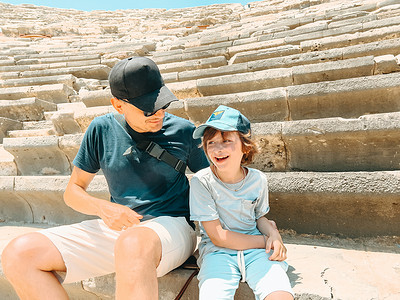 年轻的父亲和他的小学生儿子游客在炎热的夏日参观古代古董竞技场圆形剧场遗址