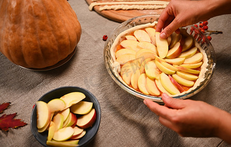 特写厨师糖果师的手将苹果片绕圈铺在烤盘卷面团上的南瓜泥上