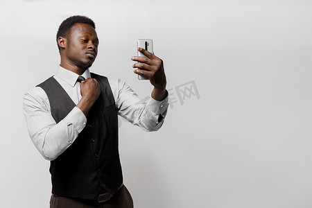 留着黑胡子的非洲人正在通过智能手机上的摄像头寻找自我，并拉直领带。