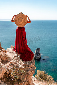 一位披散着头发、身穿红色长裙的女孩从黄色岩石间的楼梯上走下来，俯瞰着大海。