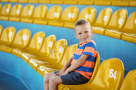 小男孩坐在空荡荡的体育场里，周围是黄色塑料麻木