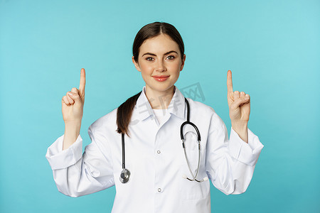 自信的年轻女医生、穿大衣的医务人员的肖像，指指点点，微笑，展示药品广告、诊所促销、托瓦石背景