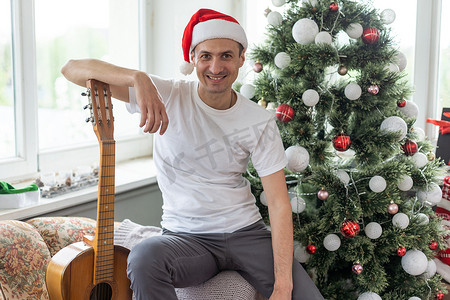 坐在沙发上的年轻帅哥，他正在弹吉他，音乐，圣诞节，放松的概念