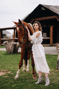 一个白色太阳裙的美丽的女孩在一个老牧场的一匹马旁边