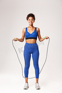 全长身穿蓝色运动服的强壮女运动员，跳绳微笑，在白色背景下做运动