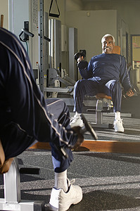 一位非裔美国老人在健身房看镜子时举起哑铃