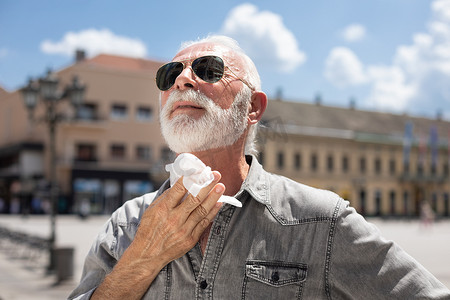 老人在户外热苏上用湿巾清洁颈部和汗水