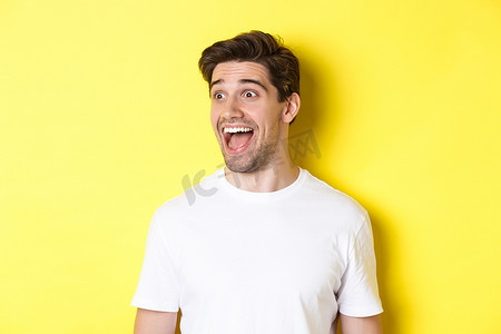 快乐男人查看促销的形象，惊讶地向左看，站在黄色背景下的白色 T 恤