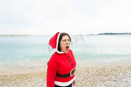 圣诞节和节日概念 — 穿着圣诞老人服装的风趣女人在大海背景下有扇子
