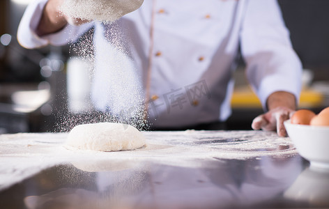 撒面粉摄影照片_厨师在新鲜的披萨面团上撒面粉