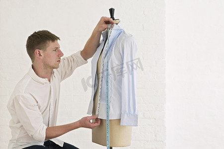 时装工作室裁缝模型上的年轻男裁缝测量衬衫