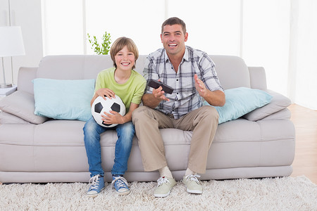 快乐的男孩和父亲坐在沙发上看足球比赛