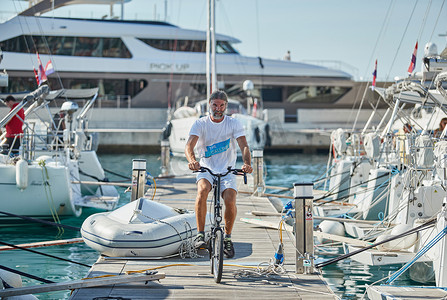 克罗地亚，斯普利特，2019年9月15日：背景是船只的帆船赛的残酷参与者在码头上骑自行车，人们正在等待即将到来的比赛、船长和水手