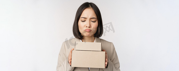 亚洲女售货员、女企业家拿着盒子，看上去悲伤、失望，站在白色背景上的肖像