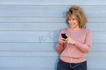 手机听音乐摄影照片_微笑的女人用耳机和手机听音乐