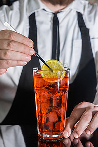 一位专业的酒保在夜总会柜台的玻璃杯中放了一片柠檬和红色冰镇酒精鸡尾酒