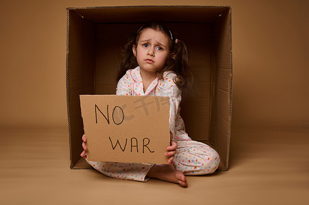 心烦意乱的欧洲小女孩坐在一个纸箱里，展示着一张停止战争的海报。