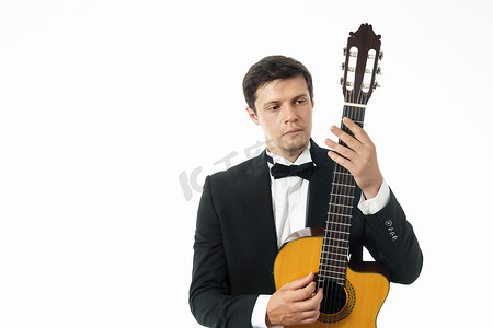 穿着黑色经典西装的年轻人拿着古典吉他合影，看着一把古典吉他的琴颈。