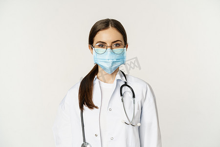 女医生、戴着眼镜和医用面罩的医院工作人员的特写，看起来很严肃，准备迎接医院病人，站在白色背景上
