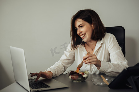 女员工在办公室吃午饭，年轻的黑发女人在工作场所吃沙拉